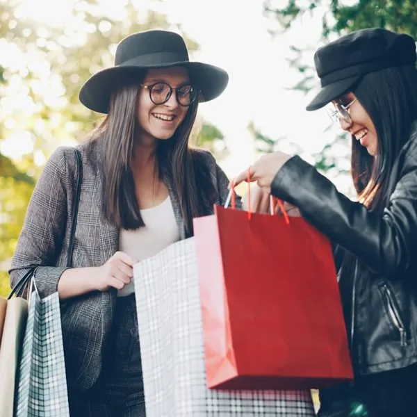Dos clientas sonrientes miran sus bolsas de compra